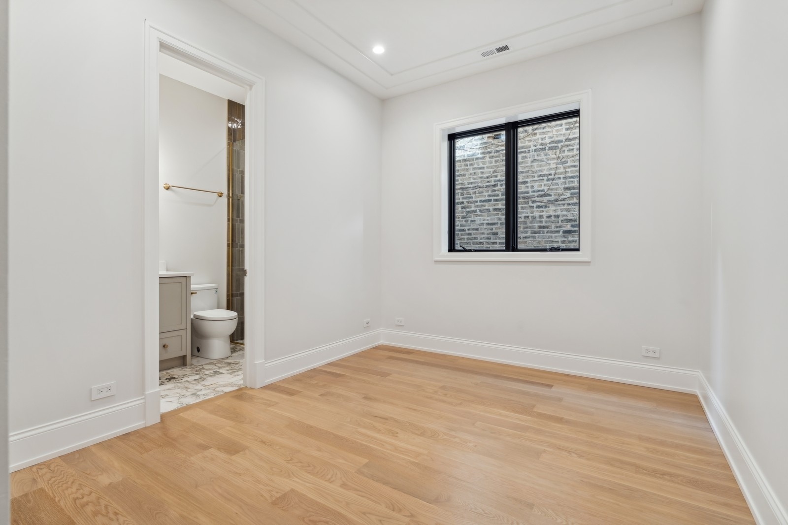 Empty bedroom with oak floors, a black-framed window, and an en-suite bathroom.