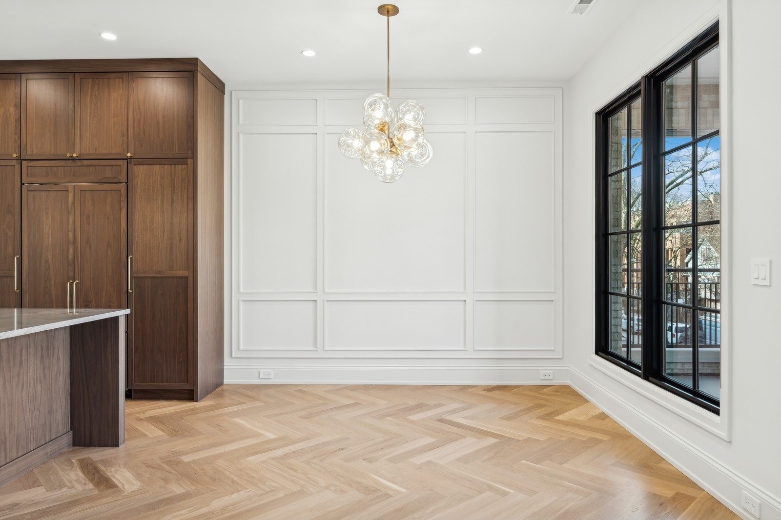 Kitchen with walnut cabinetry, herringbone floors, and tall black-framed windows.