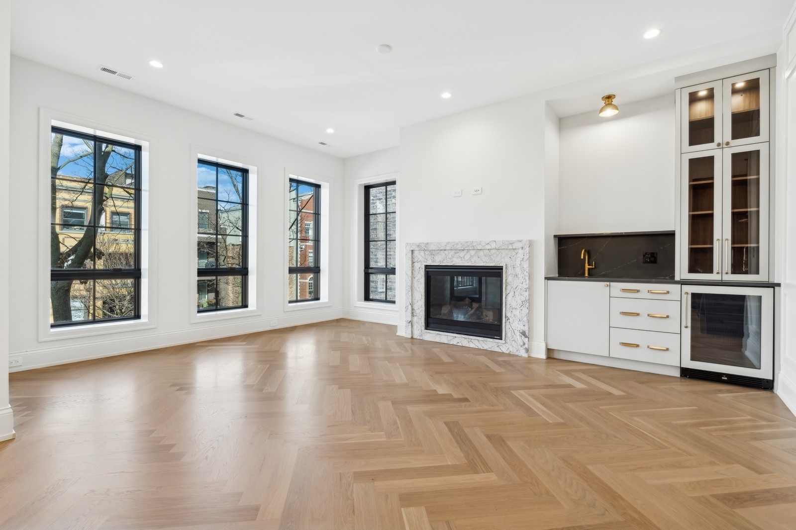 Bright living room with herringbone hardwood floors, marble fireplace, and built-in bar.