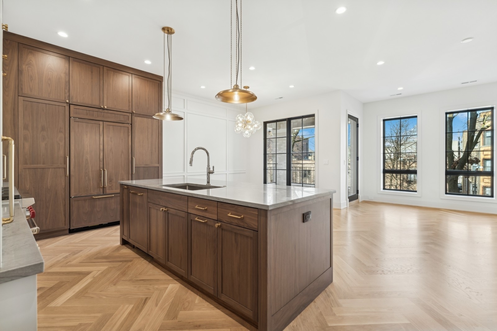 Kitchen with walnut cabinetry, a large stone island, brass pendants, and herringbone wood flooring.