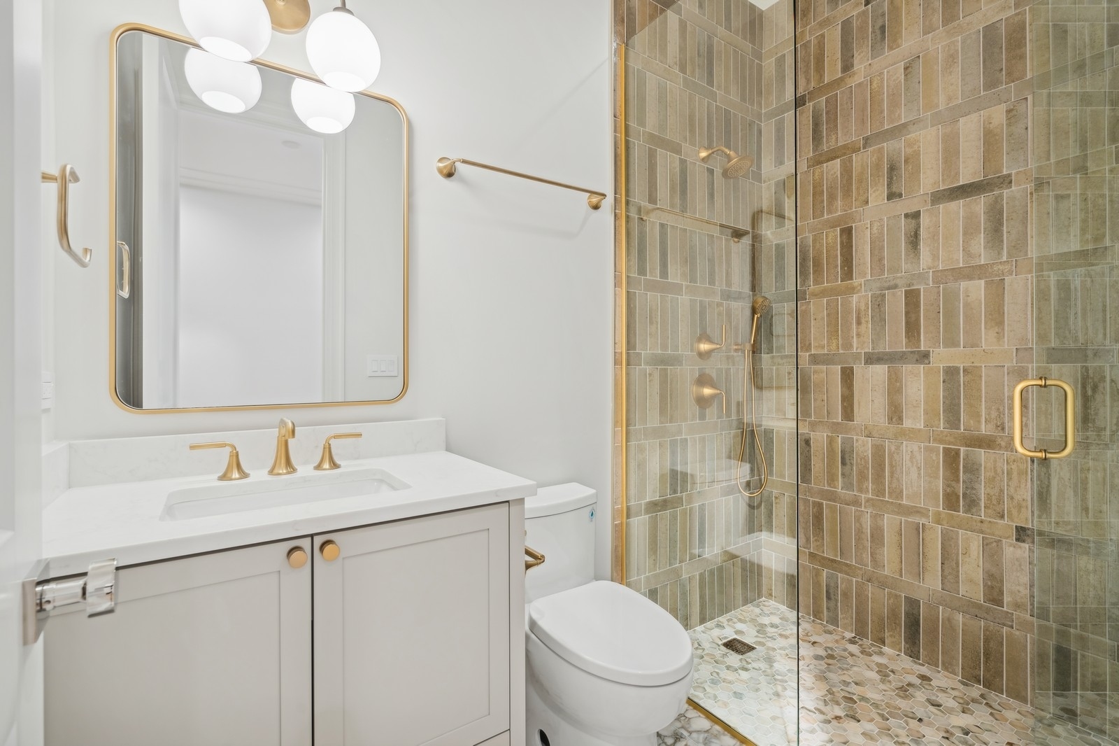 Bathroom with white vanity, gold fixtures, and a glass shower lined with beige tile.