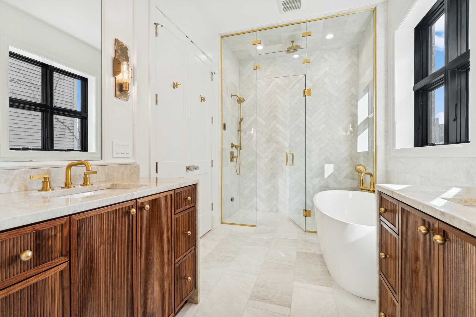 Marble bathroom with a glass shower, freestanding tub, gold fixtures, and fluted wood vanities.