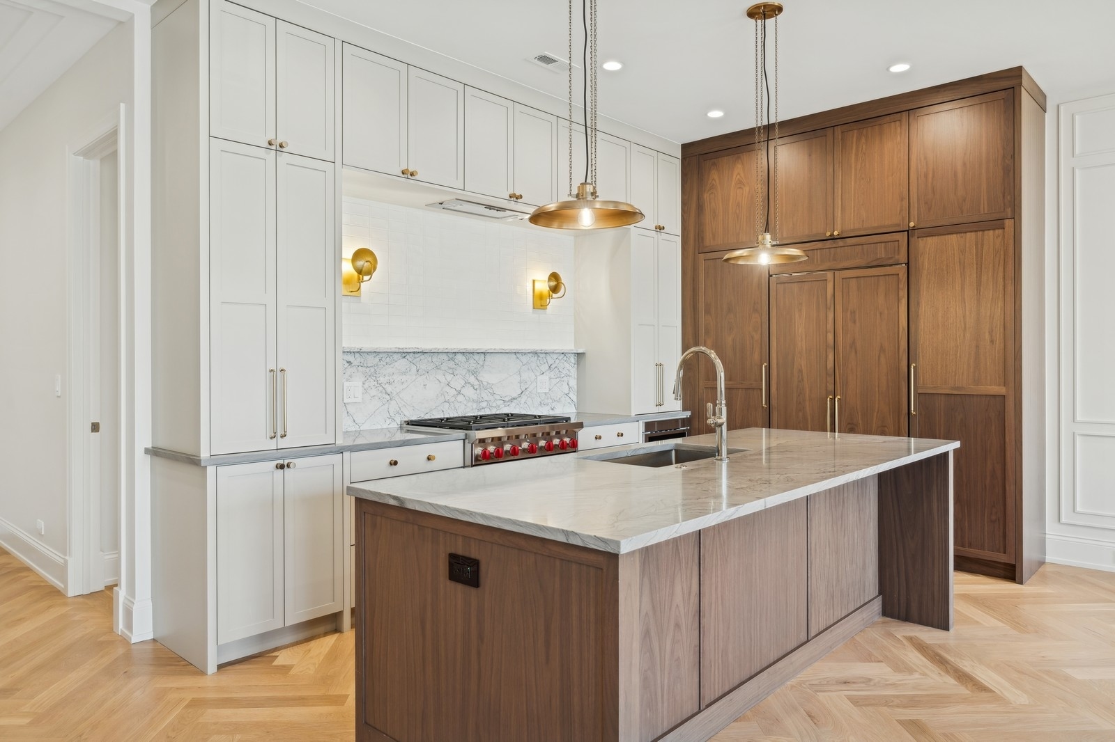Kitchen with a marble island, white and walnut cabinetry, and brass pendant lights.