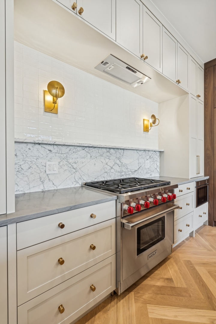 Kitchen with white cabinetry, marble counters, brass sconces, and a stainless steel Wolf range.