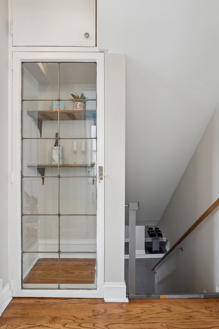 Staircase beside a white glass-paneled door with display shelves and hardwood flooring.