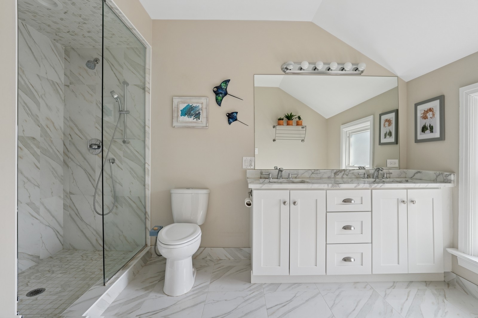 Bathroom with a marble-tiled glass shower and white double-sink vanity beneath a sloped ceiling.