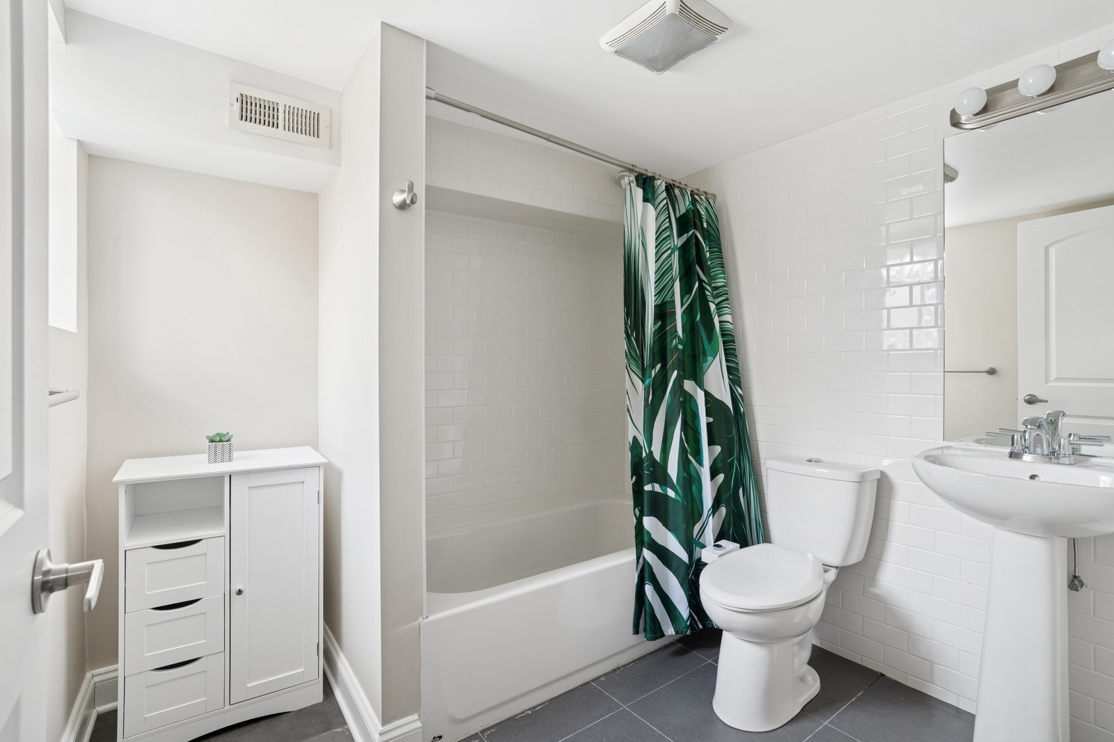 Bathroom with white subway tile, a bathtub, and a green leaf-patterned shower curtain.