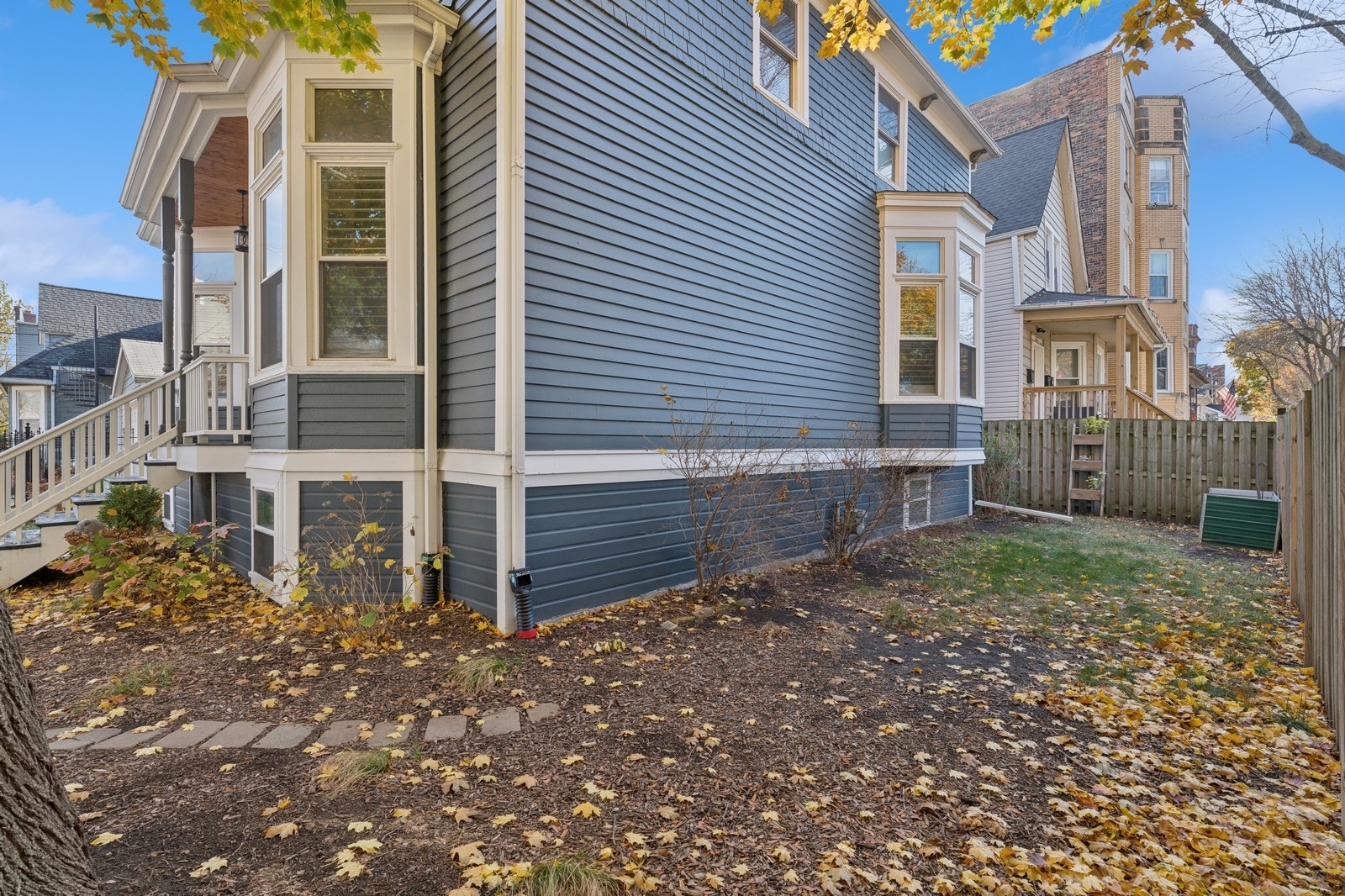 Blue-gray house with white trim beside a fenced, leaf-covered yard.