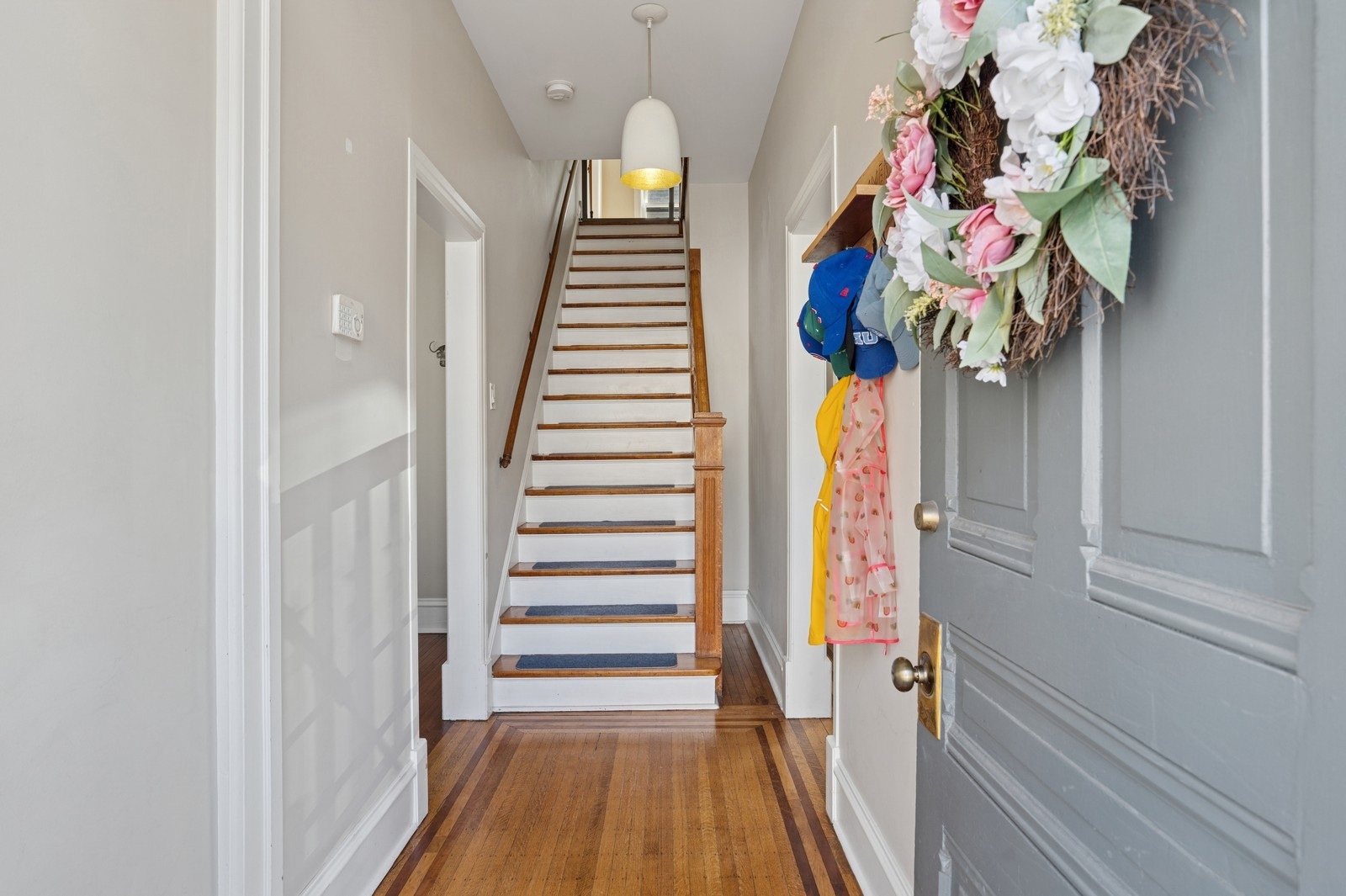 Entry hall with a wood-trimmed staircase, hardwood floors, and a floral wreath by the front door.