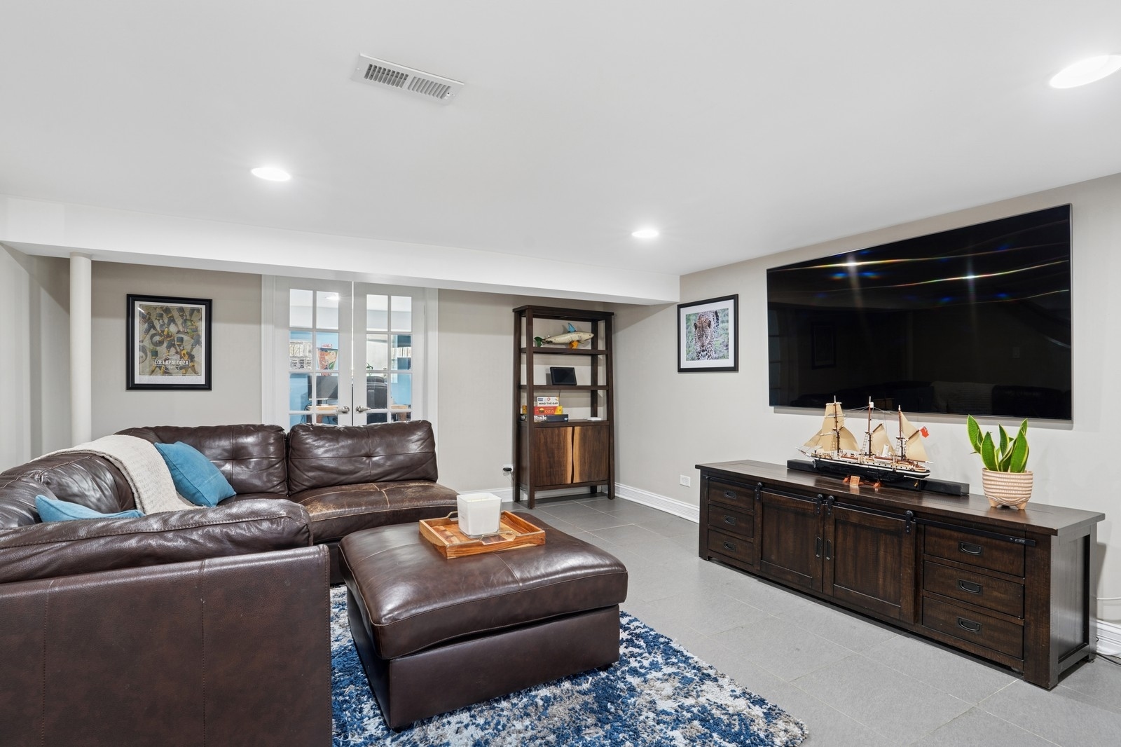 Furnished living room with a leather sectional, blue patterned rug, and large wall-mounted television.