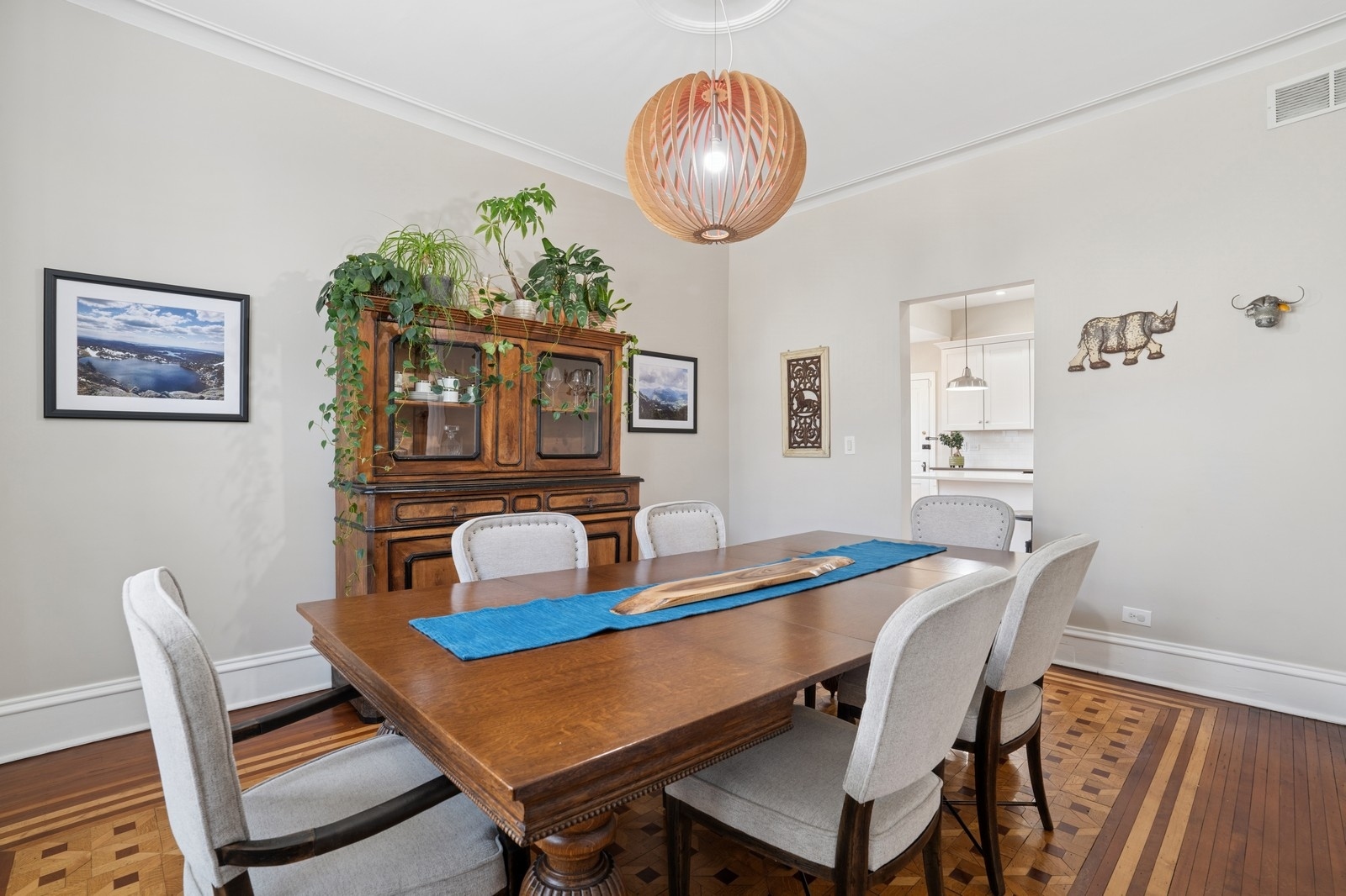 Dining room with a large wooden table, patterned parquet floor, and plant-covered wood hutch.