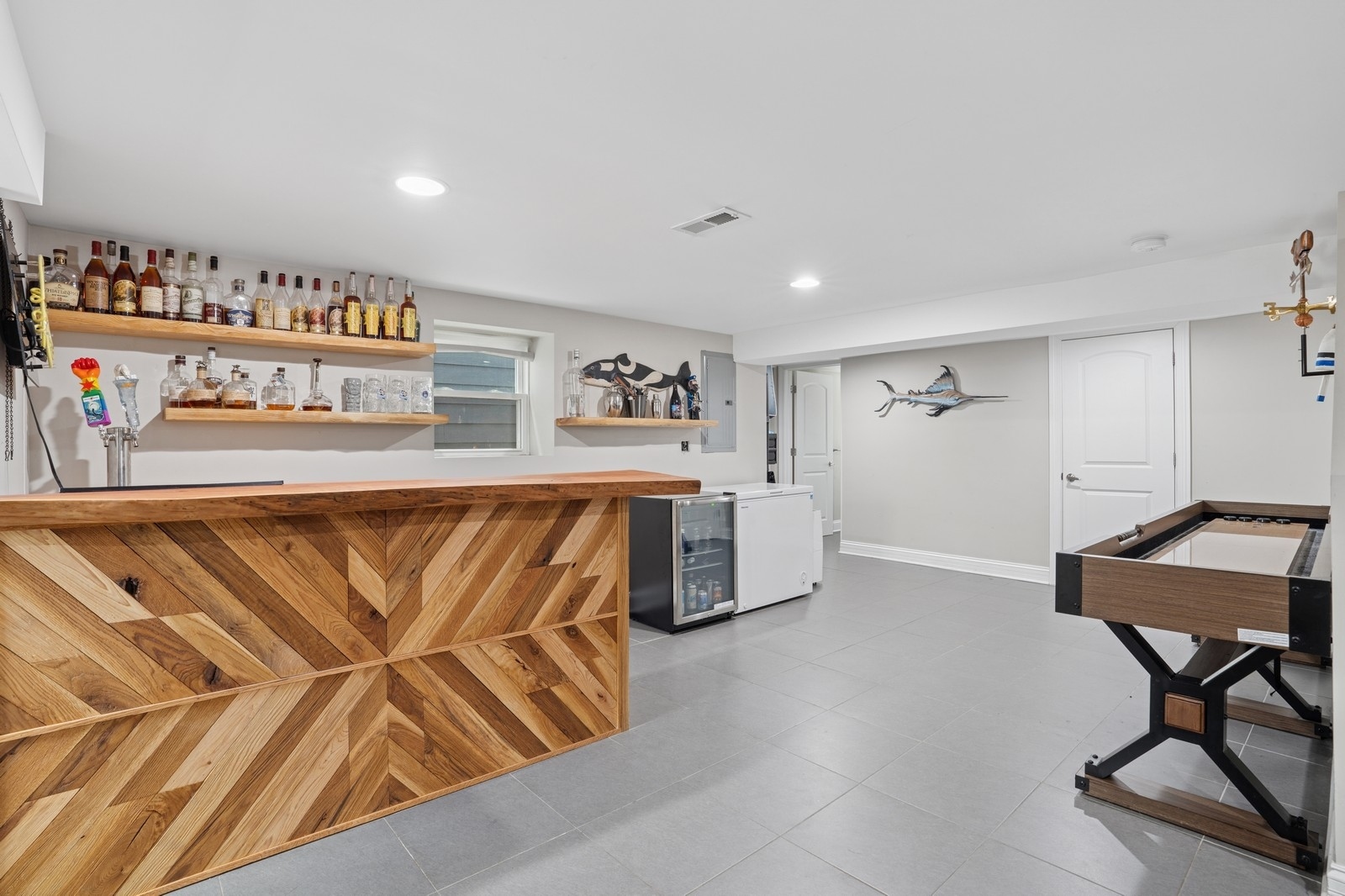 Basement recreation room with a geometric wood bar, bottle shelves, and a foosball table.