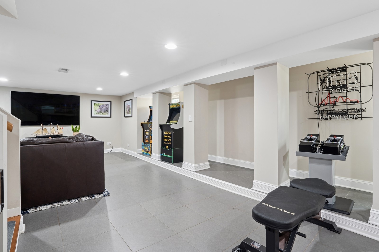 Finished basement recreation room with Golden Tee arcade games, a sofa, and workout equipment.