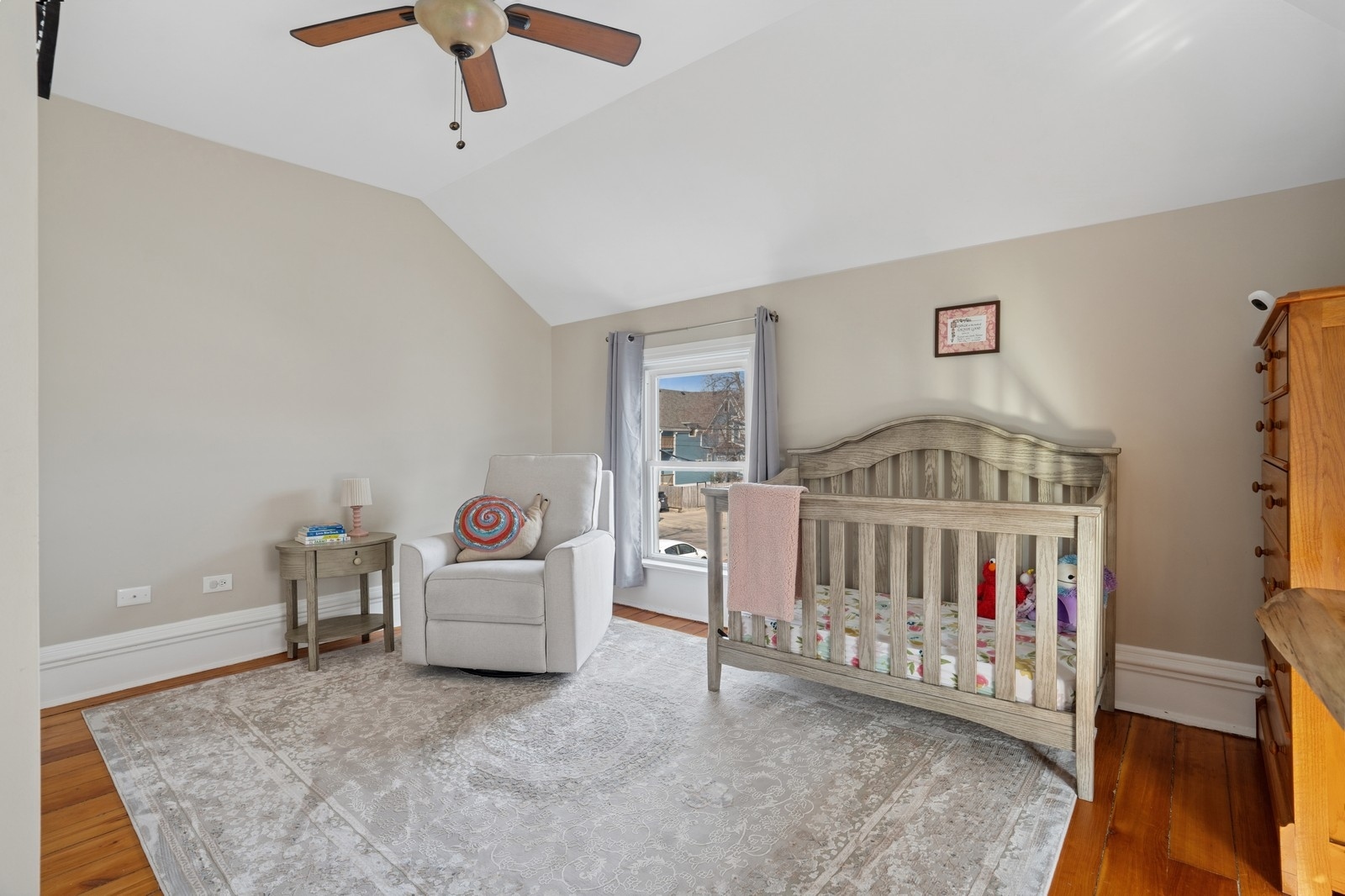 Nursery with a gray wooden crib, upholstered armchair, hardwood floors, and a large patterned rug.