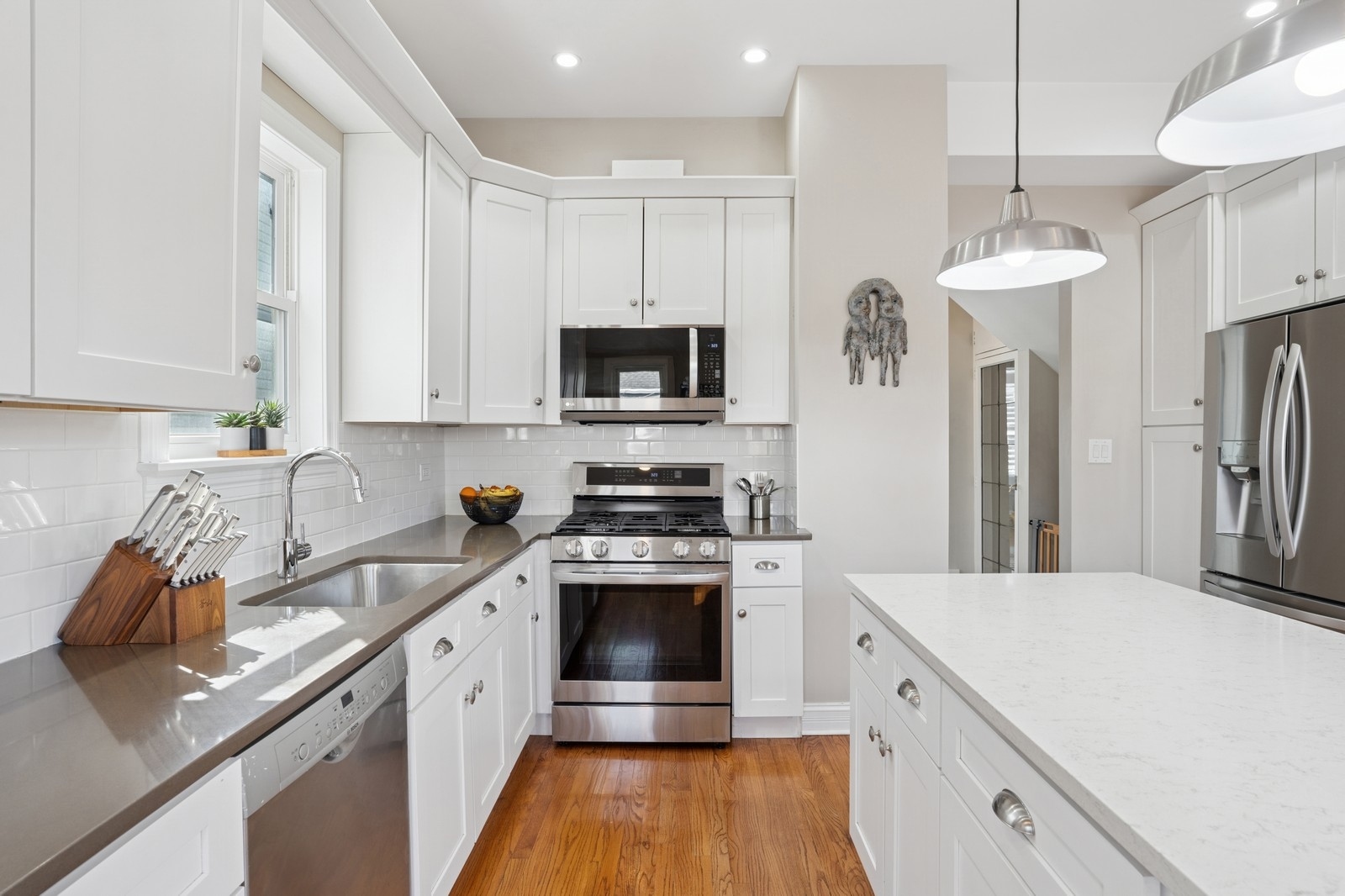 Bright white kitchen with stainless steel appliances, a large island, and warm hardwood floors.