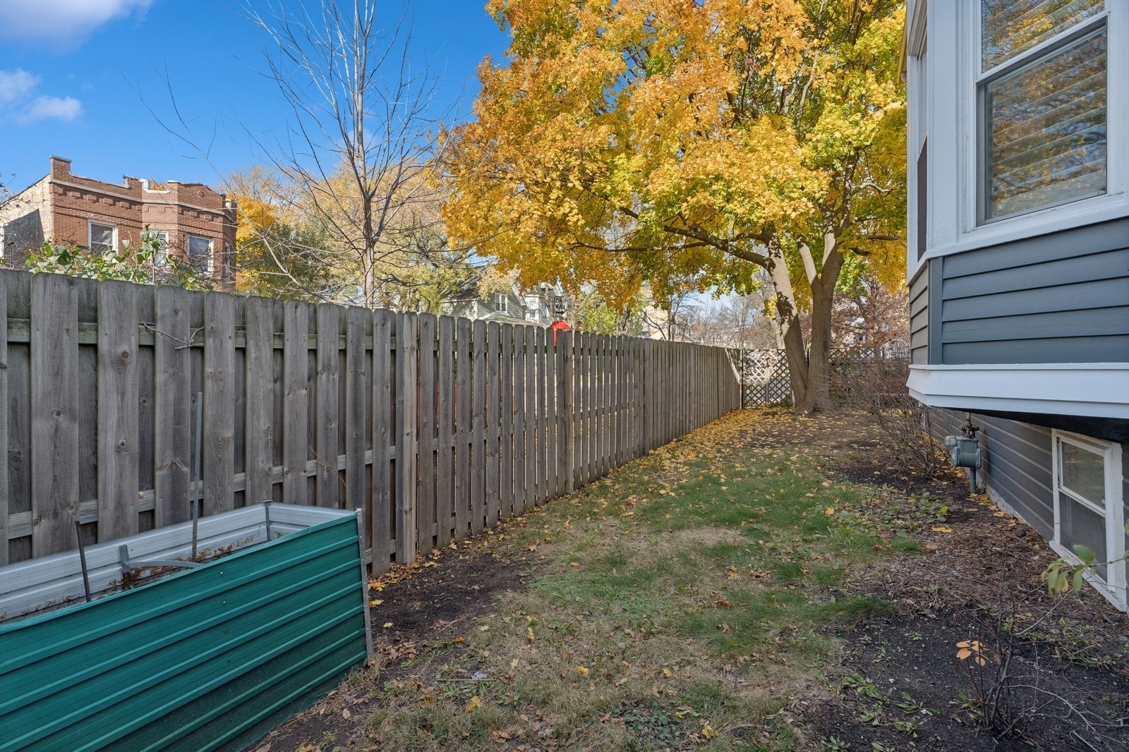 Side yard with raised garden beds, a wooden privacy fence, and a large golden-leaved tree.