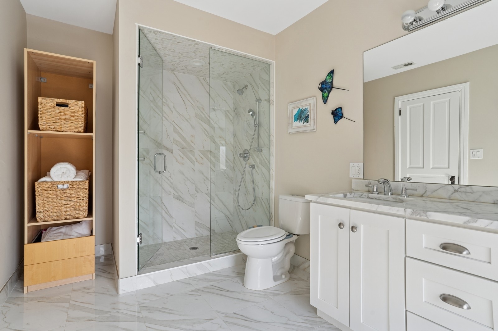 Bathroom with a marble walk-in shower, double-sink vanity, and woven baskets on open shelving.