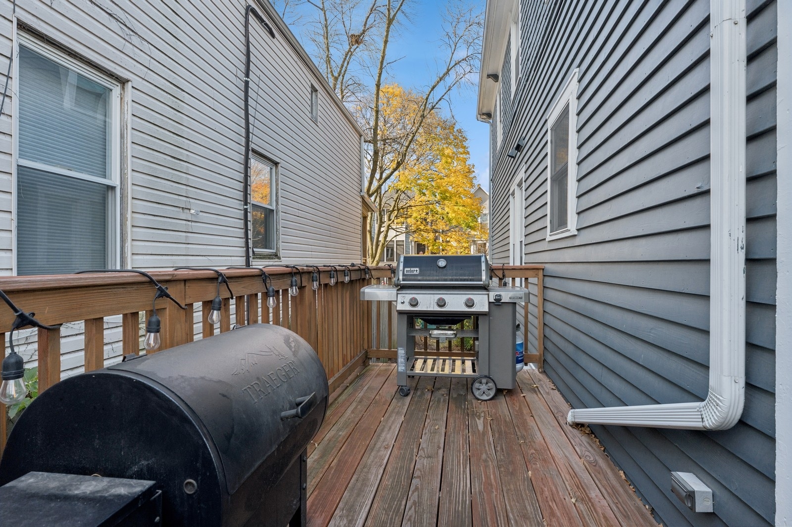 Wooden deck with string lights, a gas grill, and a large smoker between two homes.