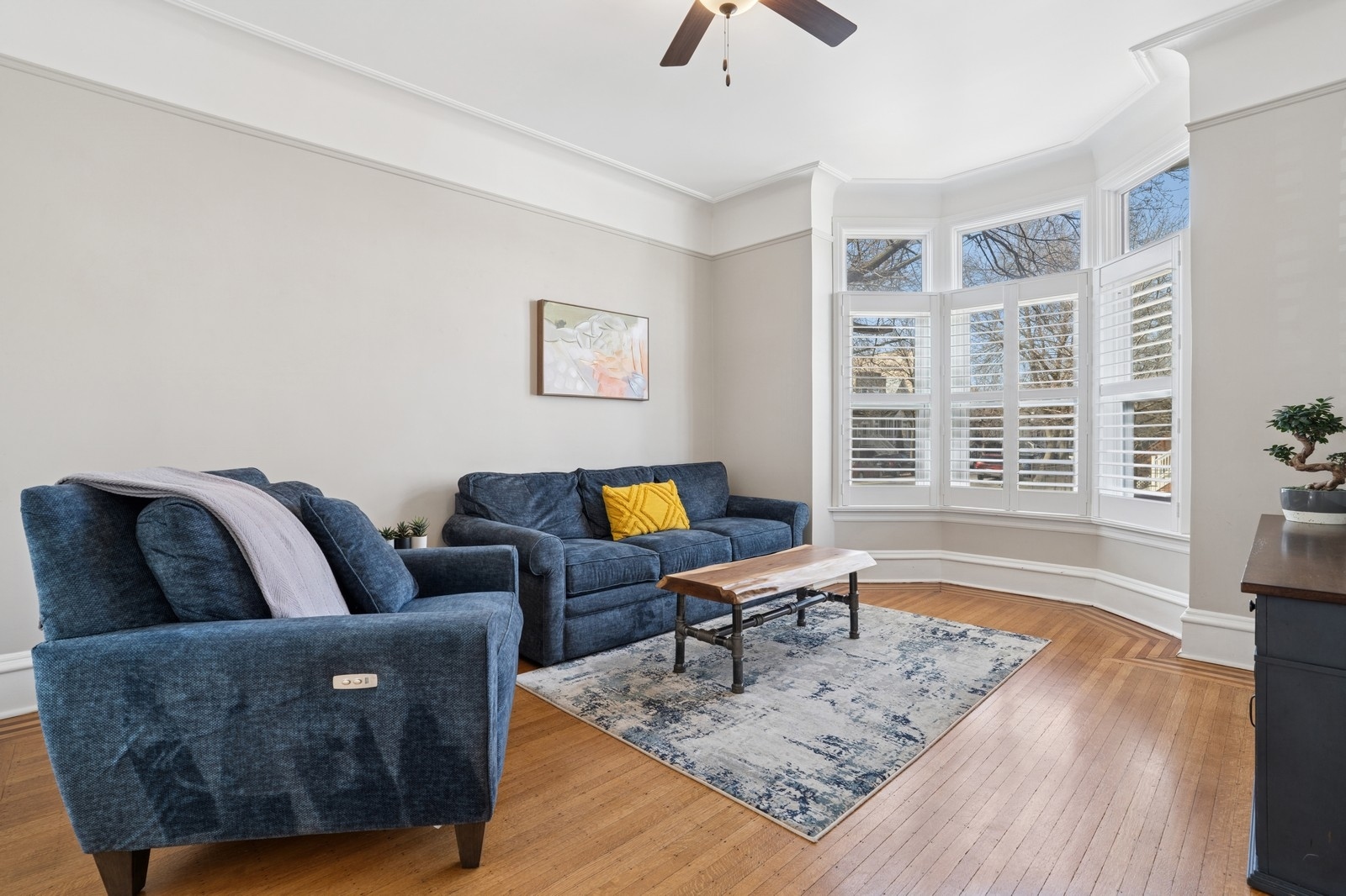 Living room with blue sofas, hardwood floors, and a shuttered bay window.