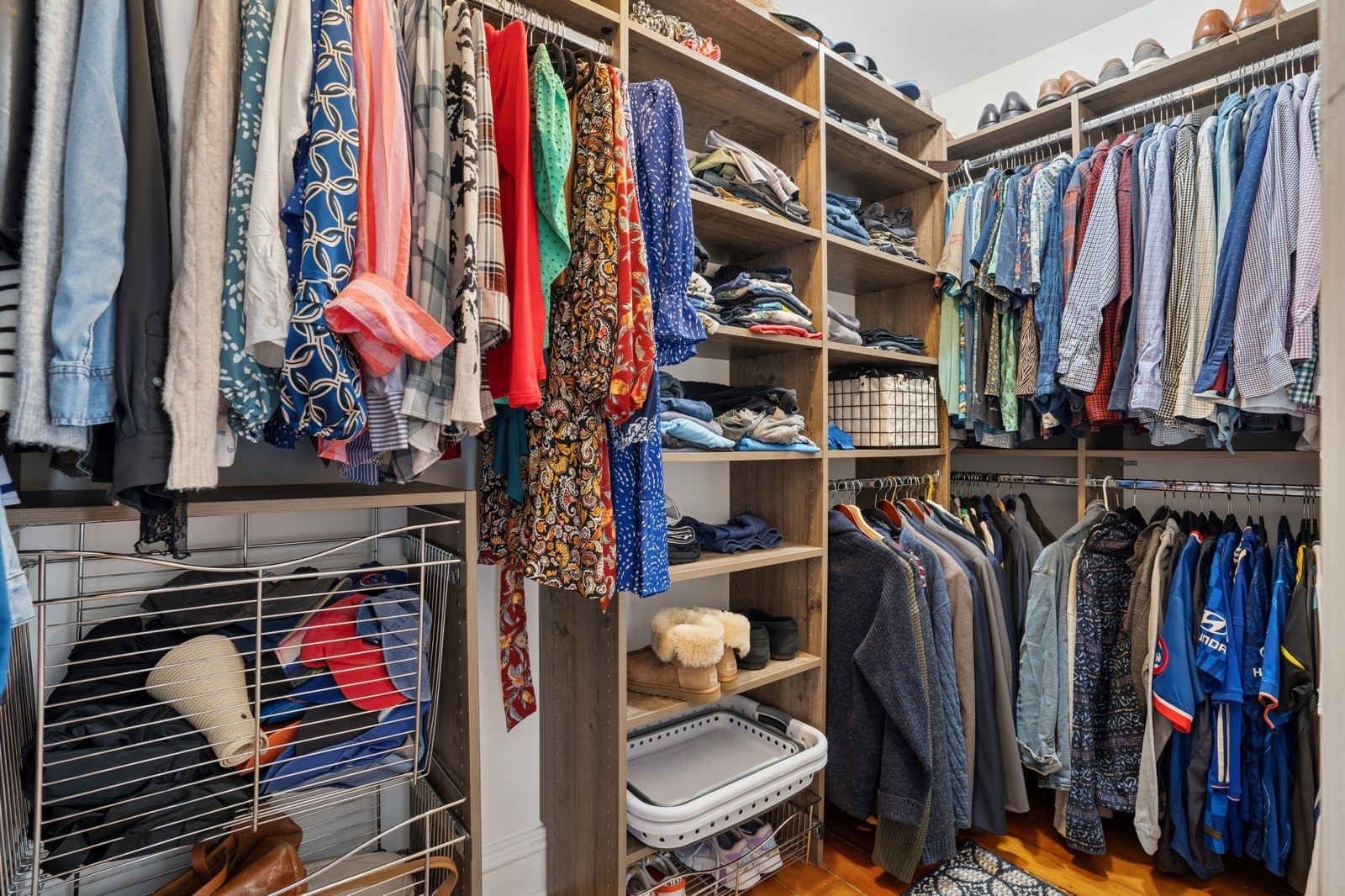 Walk-in closet with extensive wood shelving, hanging clothes, and wire storage baskets.