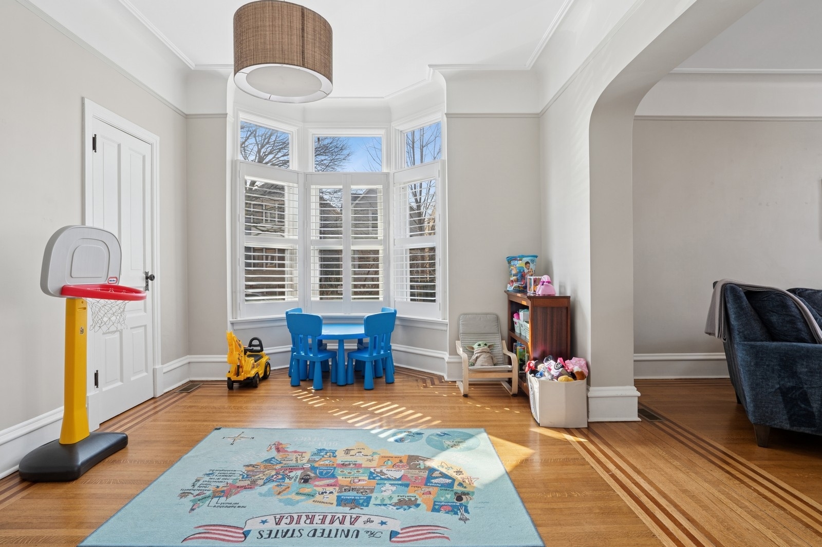 Children’s playroom with a shuttered bay window, blue table and chairs, and a map rug.