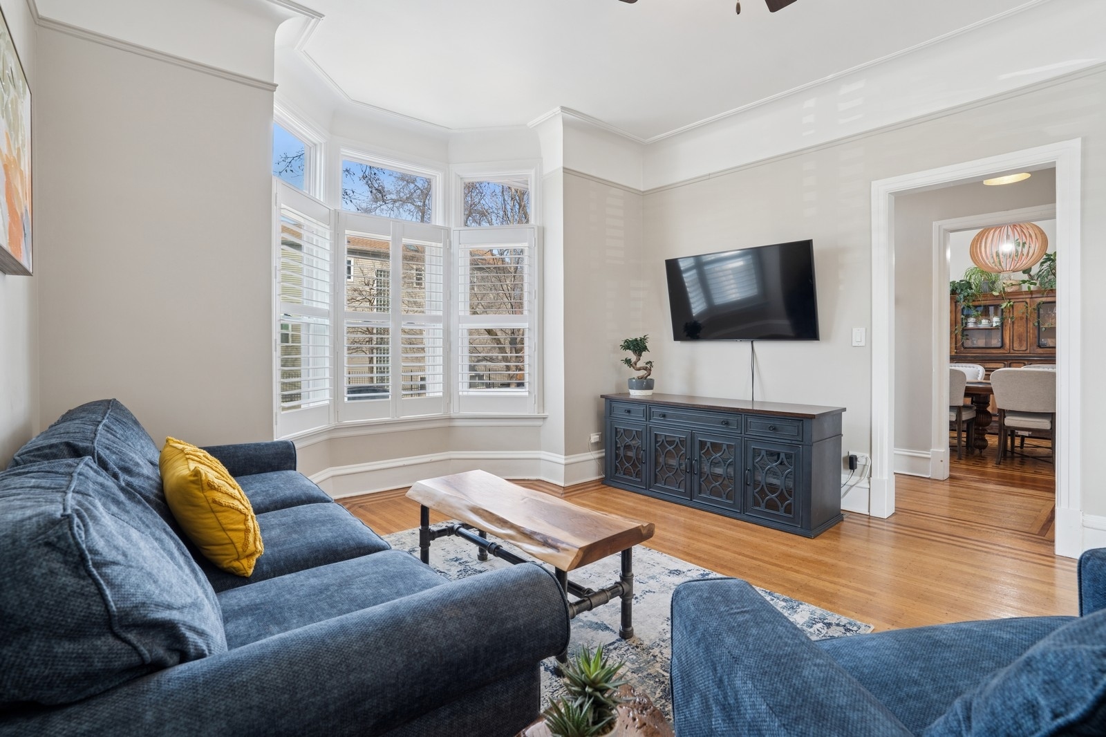 Living room with blue sofas, hardwood floors, and a bay window with plantation shutters.