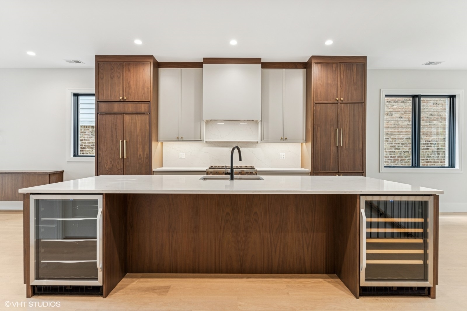 Modern kitchen with a broad stone island, walnut cabinetry, and built-in beverage coolers.