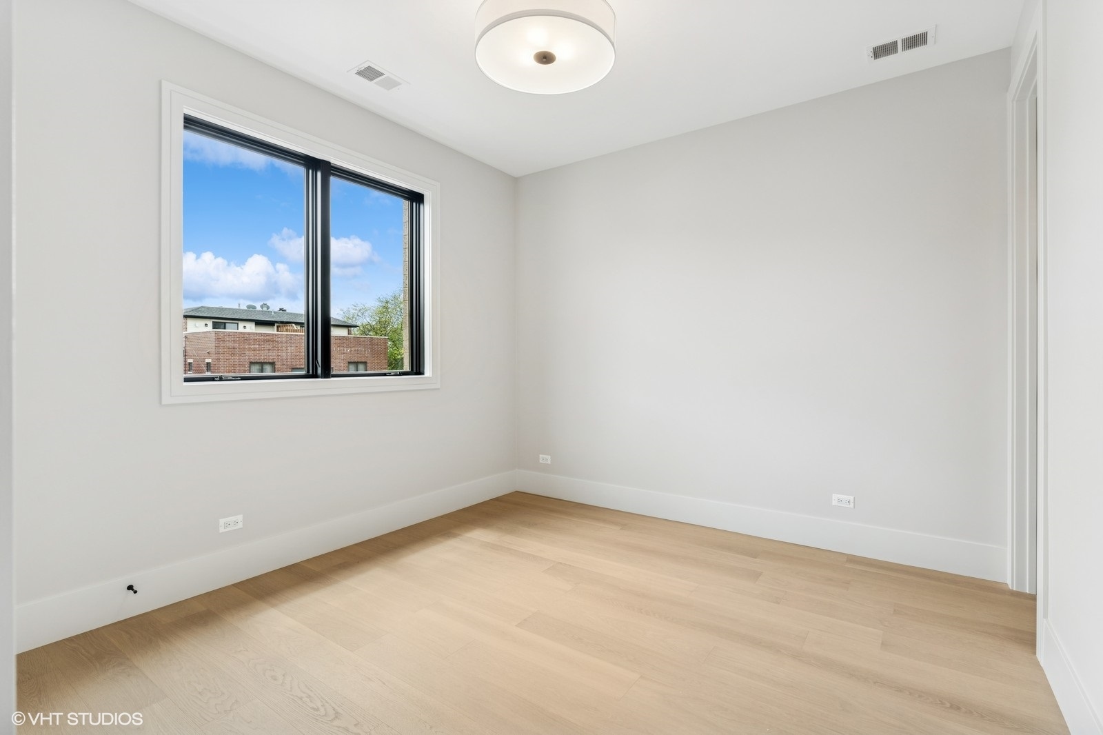 Empty bedroom with pale hardwood floors and a large black-framed window.