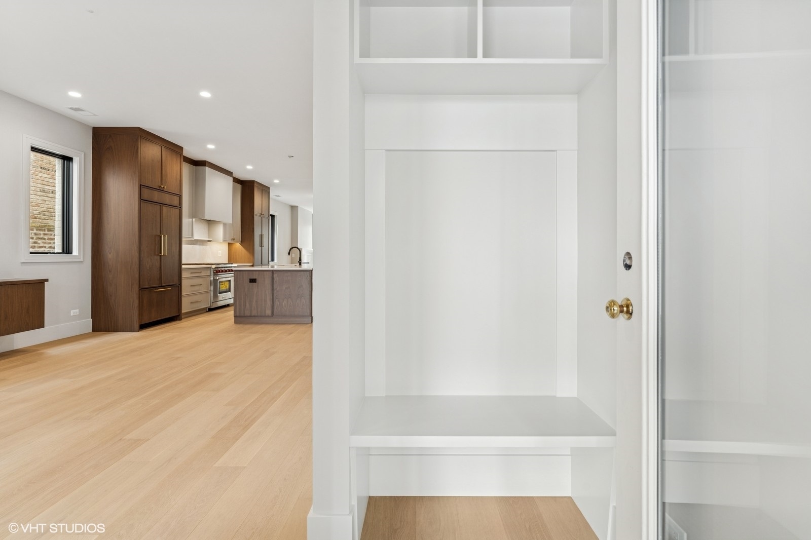 Condo entry with built-in storage, light wood floors, and a dark wood kitchen.