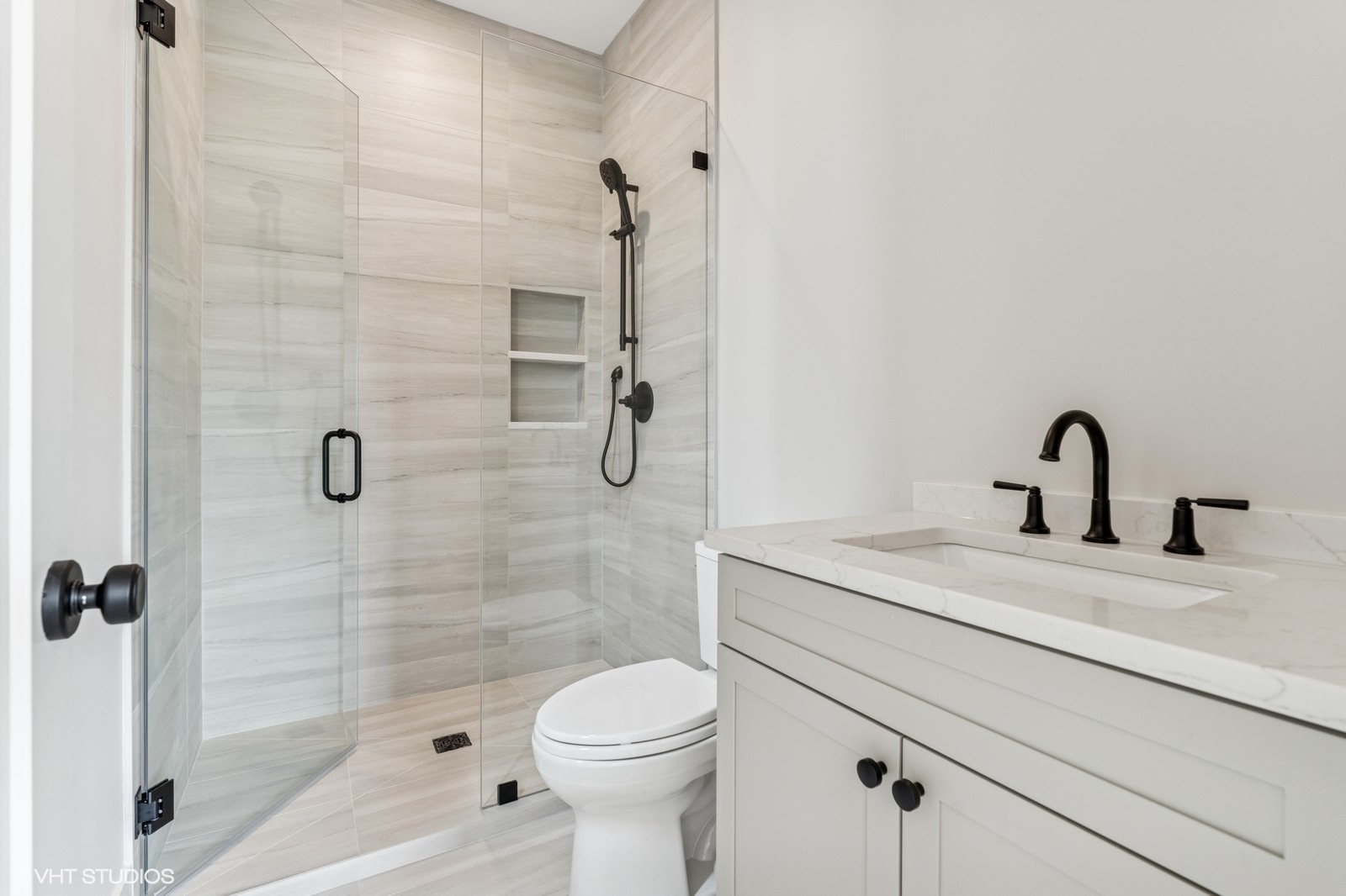 Bathroom with a marble-look glass shower, built-in niches, matte black fixtures, and a white vanity.
