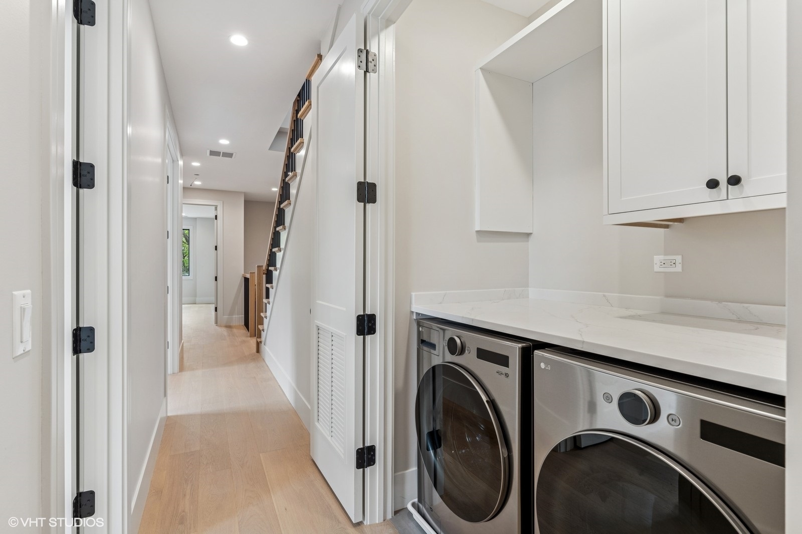 Laundry area with stainless washer and dryer, white cabinets, and a hallway leading to the staircase.