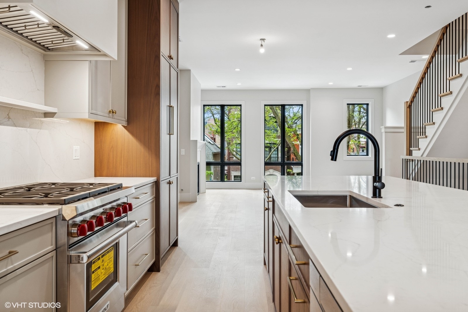 Bright kitchen with marble counters, a professional range, oversized island, and staircase beside tall windows.