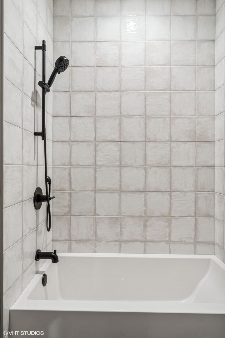 Bathtub with light gray tile and matte black shower fixtures.