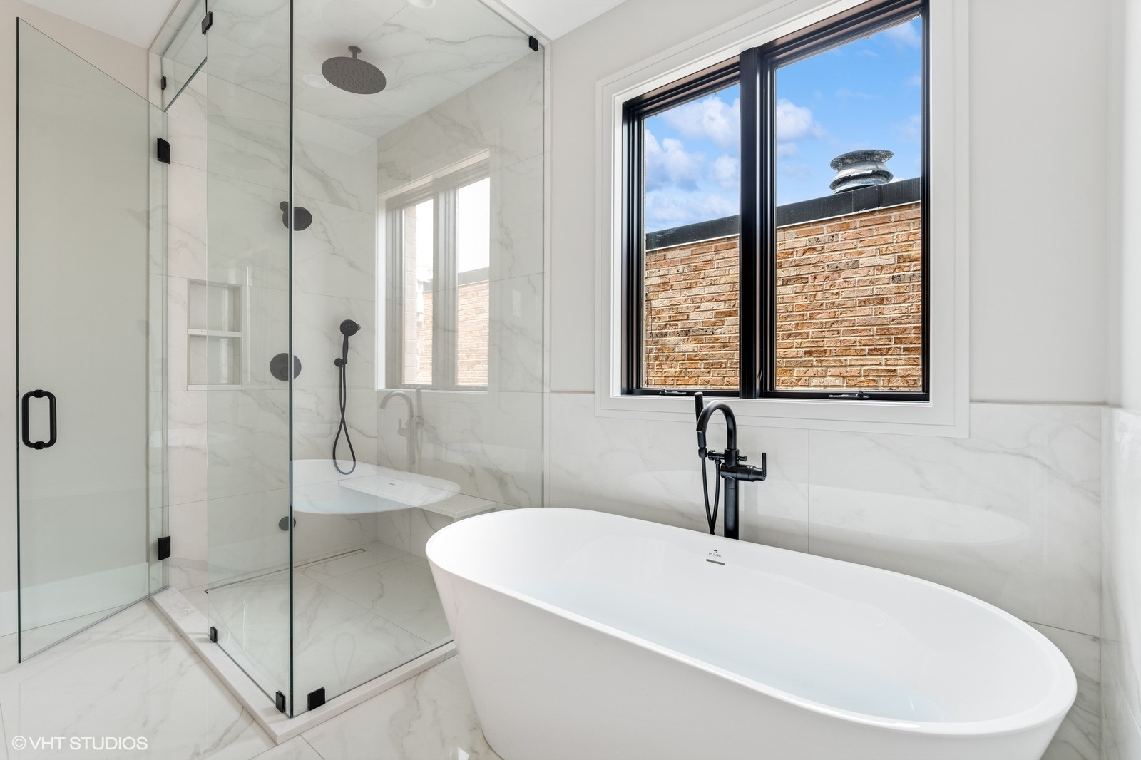 Bathroom with a freestanding tub, glass-enclosed shower, marble-look tile, and black fixtures.