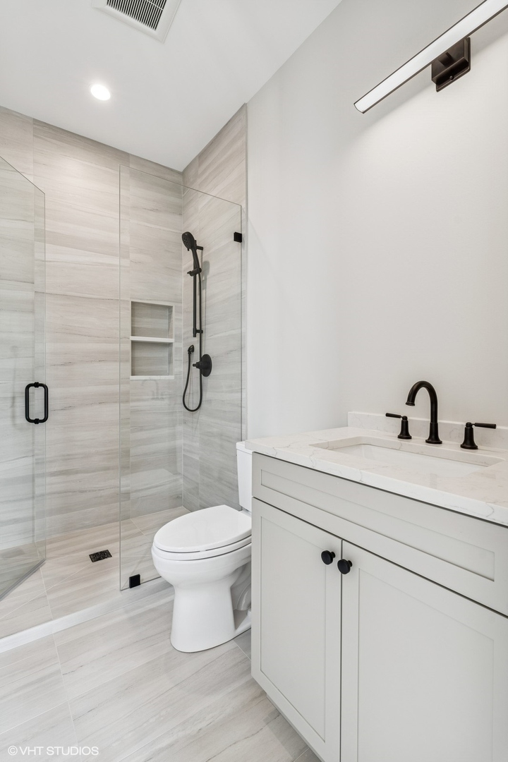 Bathroom with a glass-enclosed tiled shower, white vanity, and matte black fixtures.