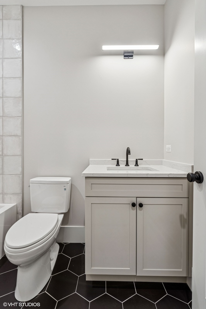 Bathroom with a light vanity, black hexagonal tile floor, and white toilet.