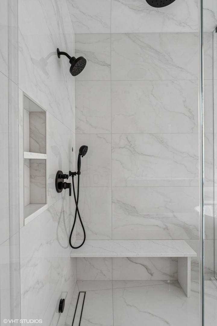 Walk-in shower with marble-look tile, matte black fixtures, a built-in bench and recessed niche.