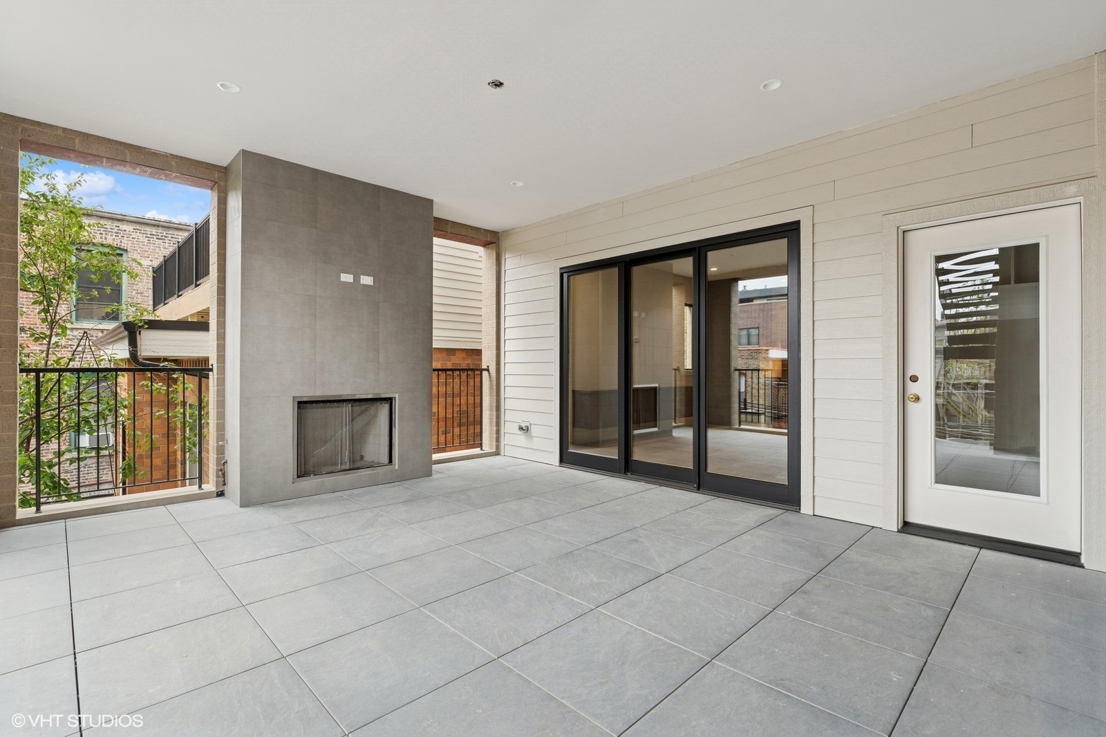 Covered terrace with tiled floor, built-in fireplace, and black-framed sliding glass doors.