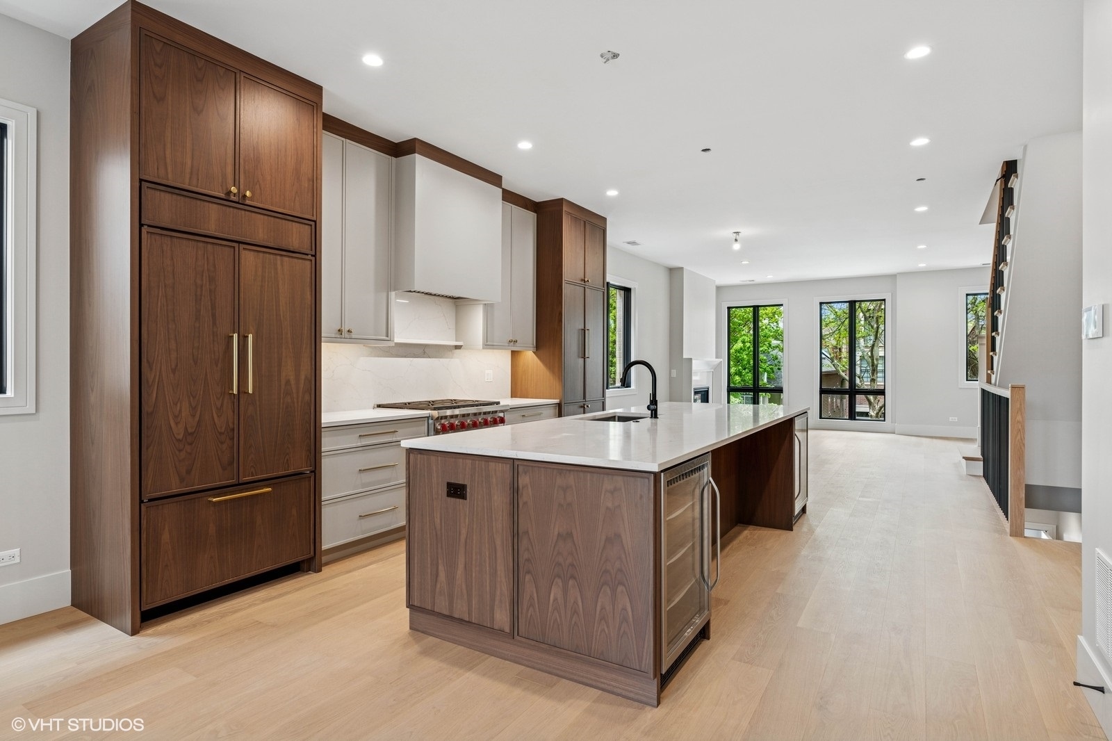 Modern kitchen with a large wood-paneled island, white counters, and tall windows overlooking trees.