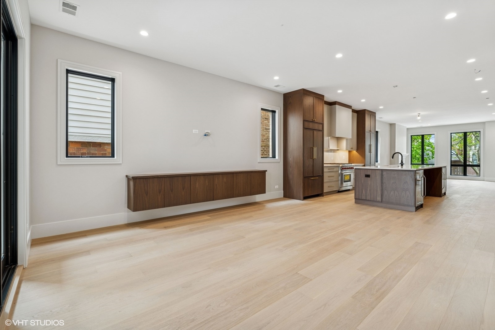 Open-plan kitchen and living area with a walnut island, pale wood floors, and large windows.