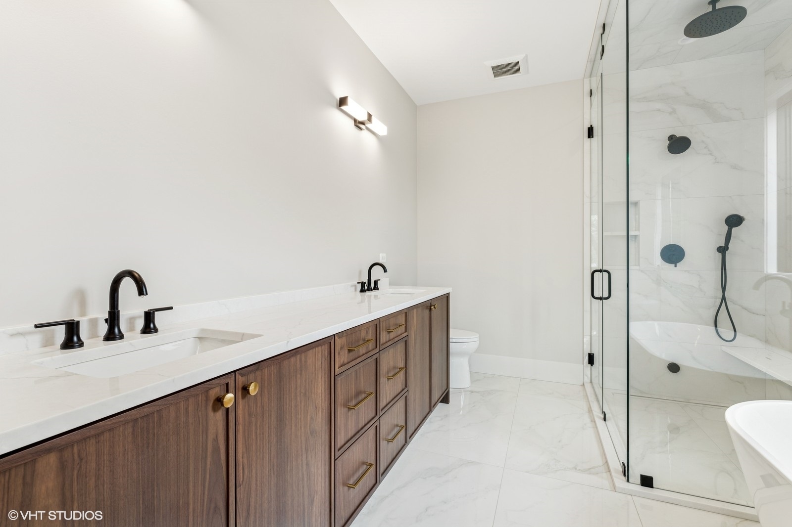 Bathroom with a long walnut double vanity and a glass-enclosed marble shower.