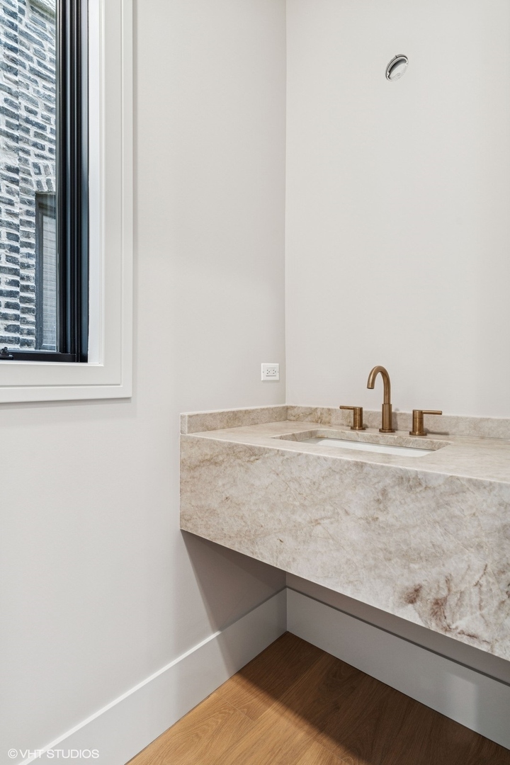 Bathroom vanity with a veined stone counter, bronze faucet, and window overlooking brickwork.