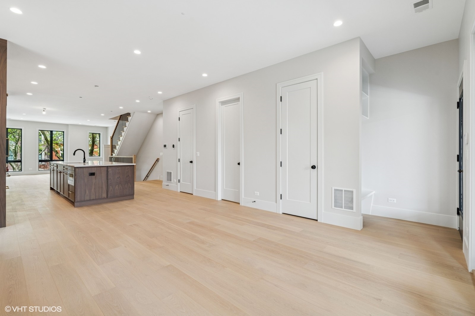 Open-plan kitchen and living area with a dark wood island, pale floors, and staircase.