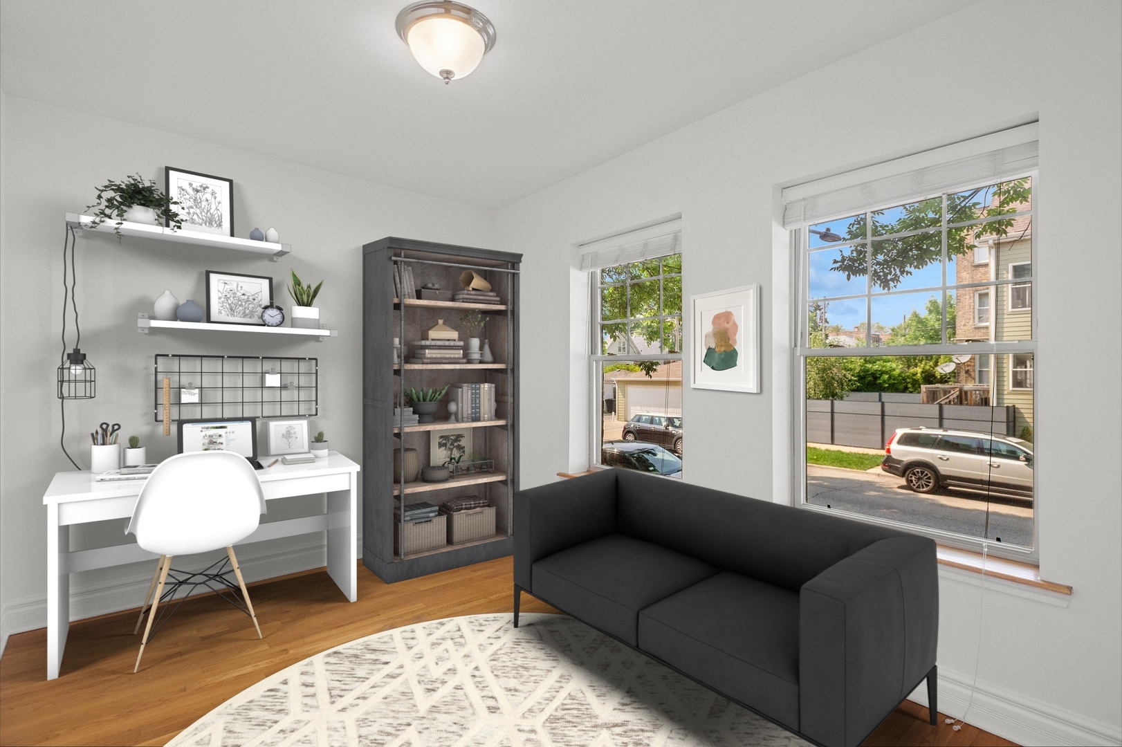 Furnished living room and office with a dark sofa, white desk, and large street-facing windows.