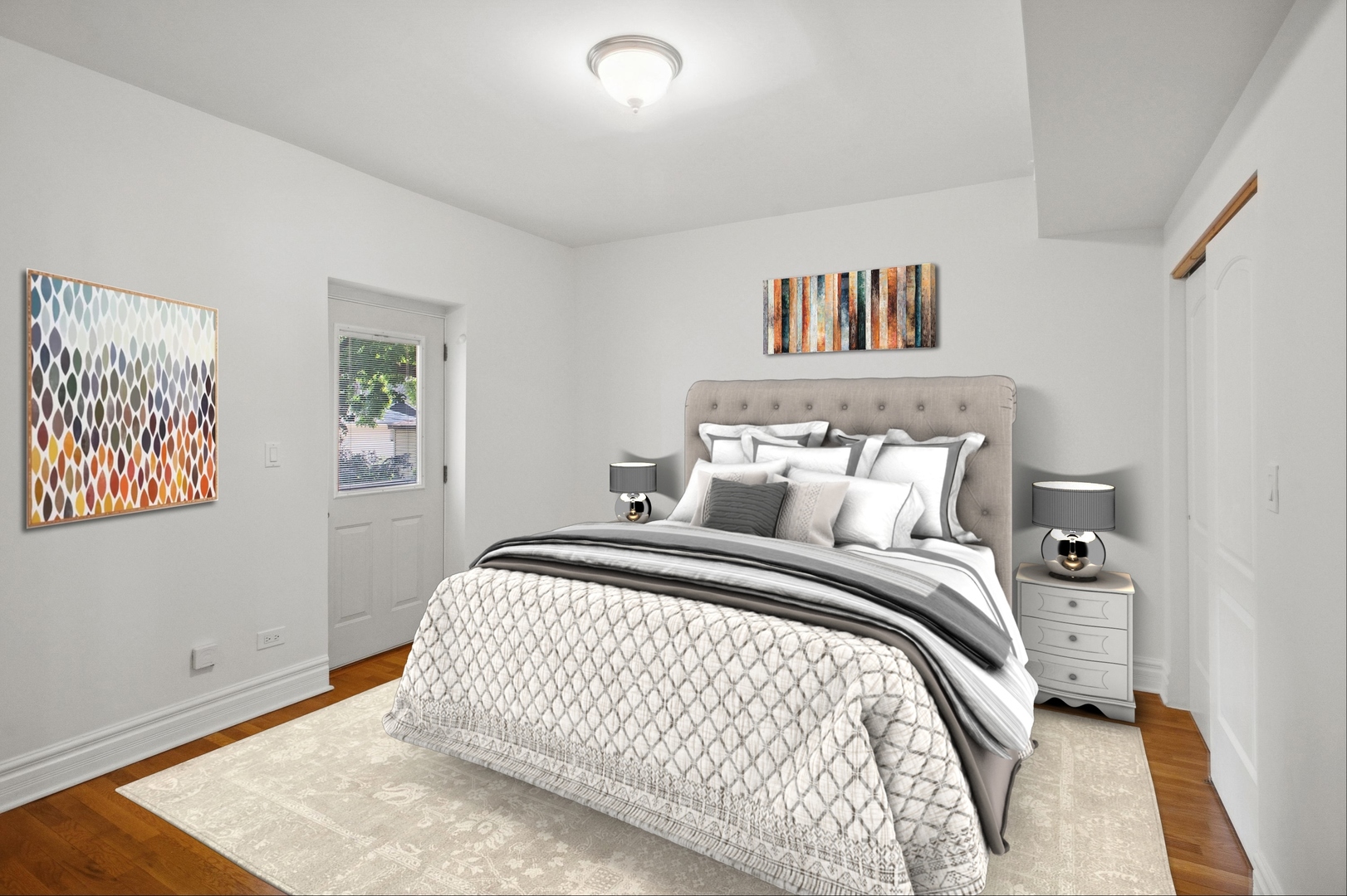Staged bedroom with a large bed, gray and white bedding, matching nightstands, and hardwood floors.