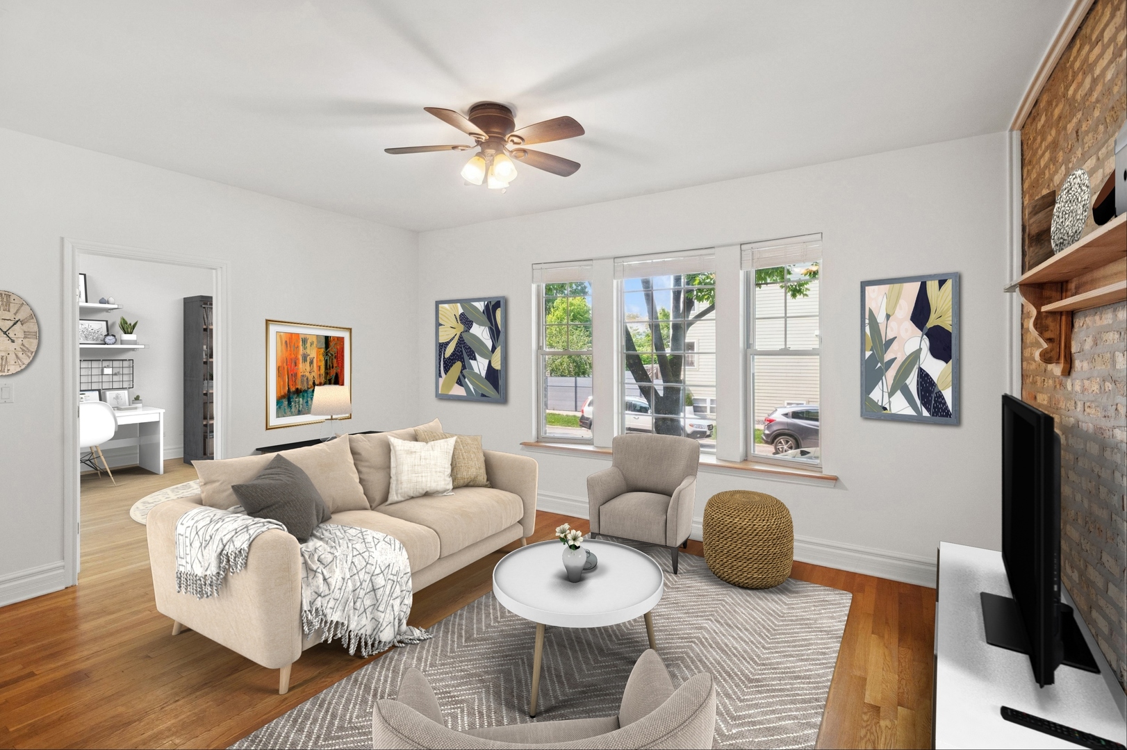 Living room with beige sofa, large windows, wood floors, and exposed brick television wall.