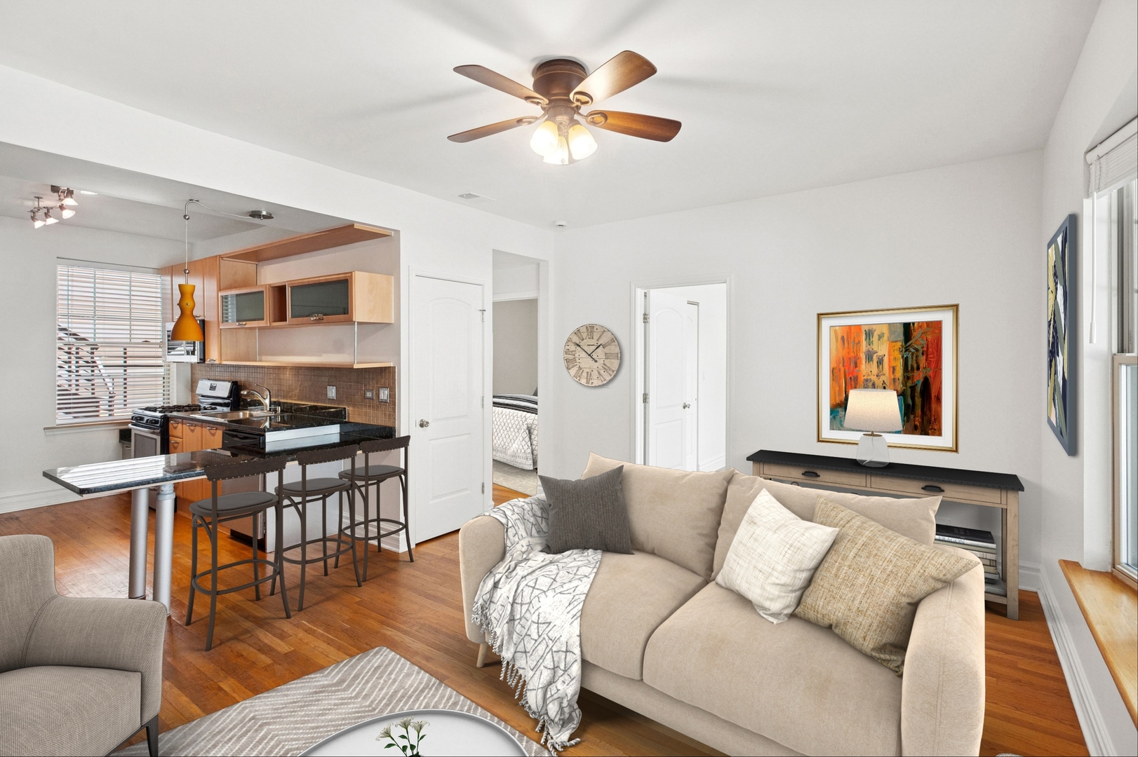 Open-plan living room and kitchen with a beige sofa, breakfast bar, and hardwood floors.