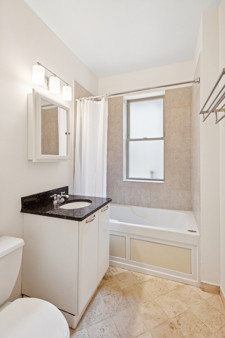 Bathroom with a white bathtub, frosted window, and vanity topped with dark stone.