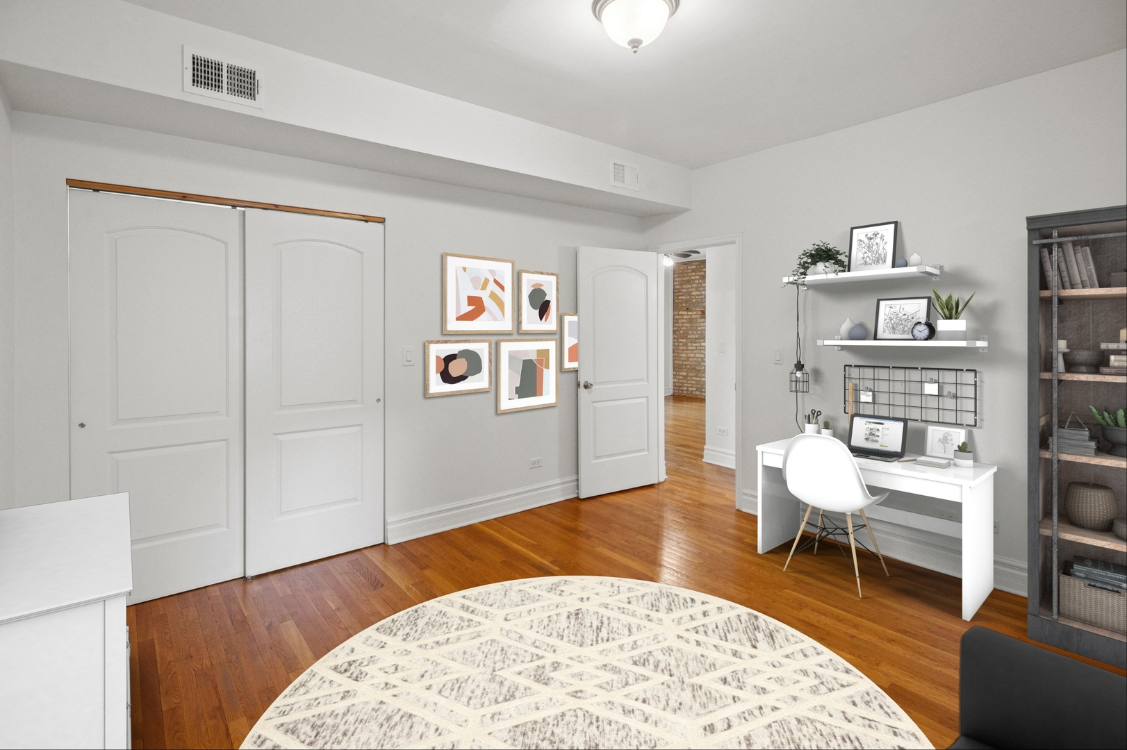 Staged room with hardwood floors, white closet doors, and a desk beside a tall bookcase.