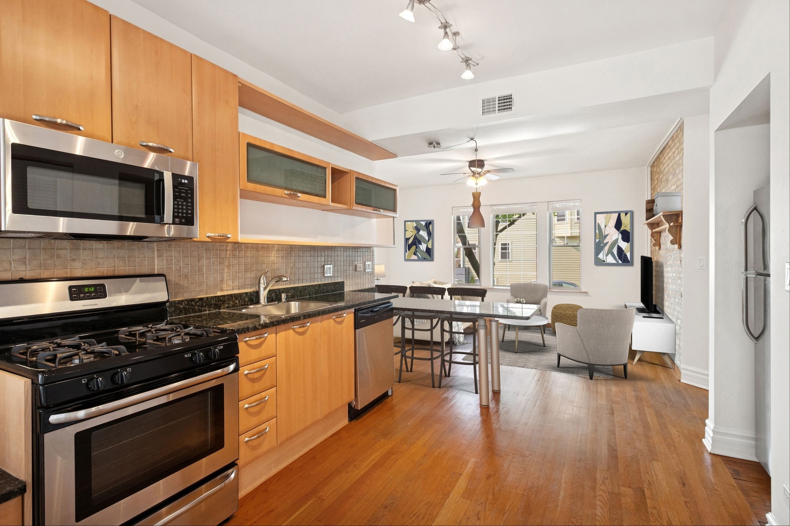 Open-plan kitchen with wood cabinets and stainless appliances opening to a dining area by the windows.